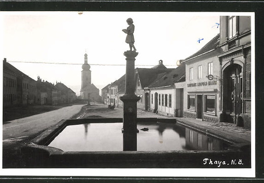 AK-Thaya-Marktplatz-mit-Brunnen-Kaufhaus-Leopold-Hainz-und-Blick-zur-Kirche